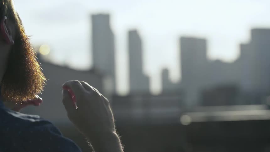 A man faces away from camera looking at a city and rubs his beard