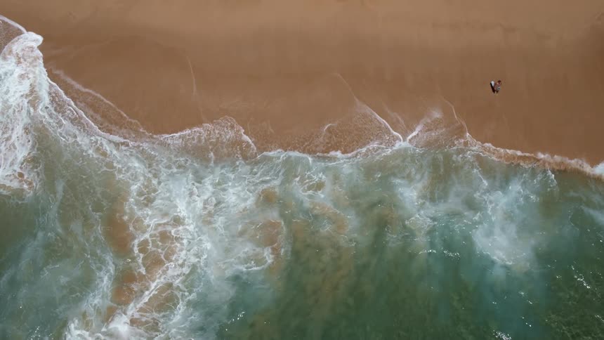 Overhead view of waves crashing on the shoreline at the beach