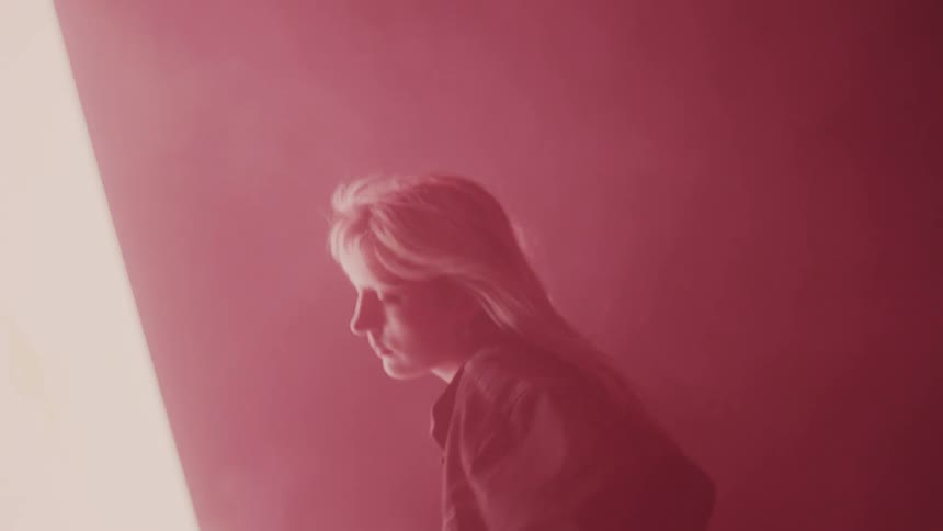 A model moves her face and shoulders around as wind moves through her hair as she poses in front of a projection screen