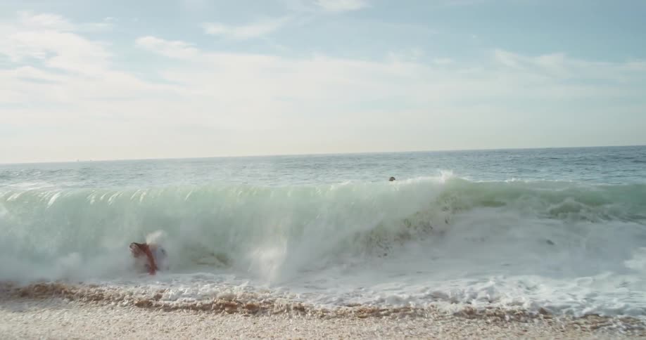 Surfer rides a big splashing wave into the beach near a rock formation