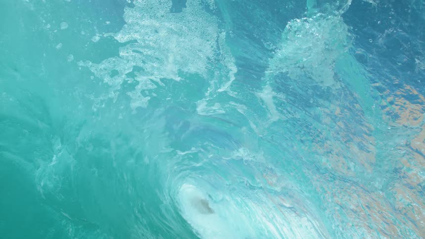Large clear water ocean wave cascading forwards towards the shore of a beach at daytime