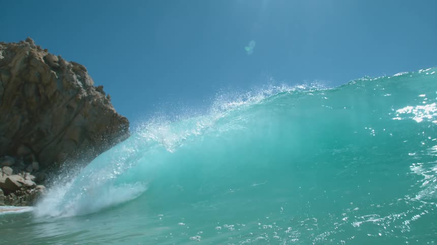 Big blue wave splashes as it rolls in under a clear blue sky