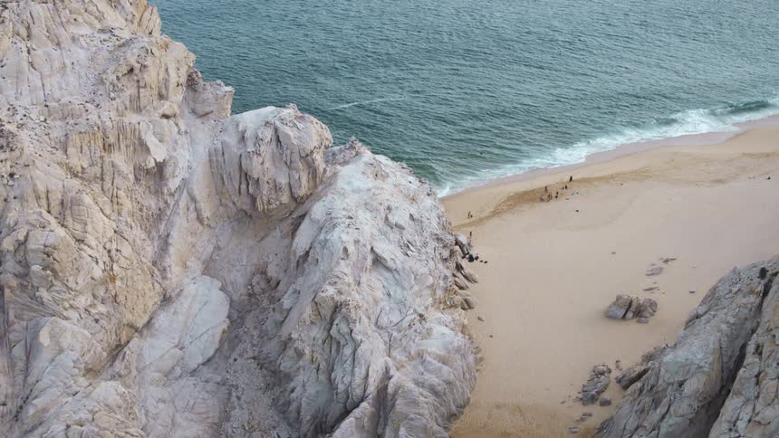 Group of people sitting on the sand beach next to the ocean between two rock escarpments