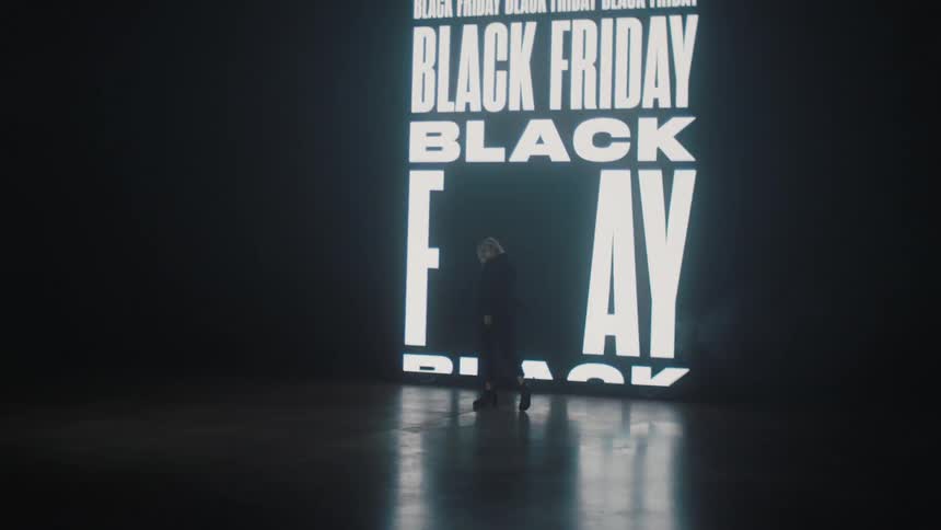 Silhouette of a woman modeling in front of a black friday sign projected on the wall of a smoky dark room