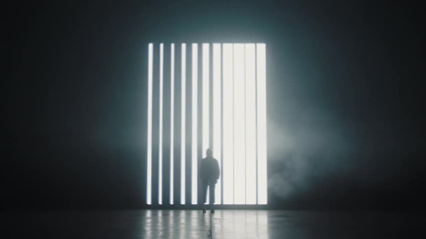 A silhouette of a person standing with a large window and blinds in the background