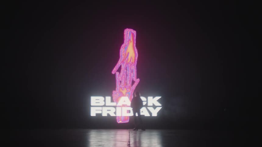 A silhouette of a person walking on a stage with a big screen in the background