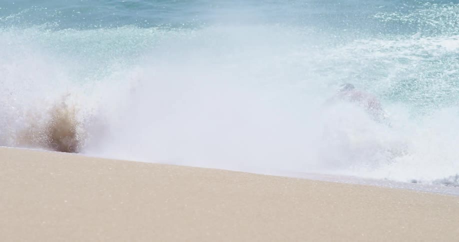Surfer rides a big blue splashing wave onto the beach