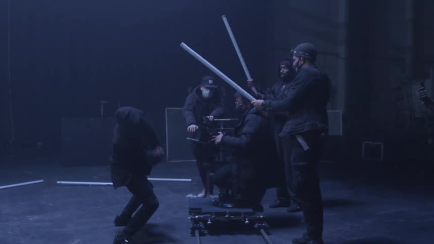 A person dancing in front of a camera being filmed by a crew inside a dark warehouse