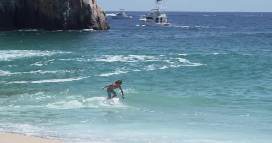 A man runs to the ocean and jumps on his surf board riding waves across the beach