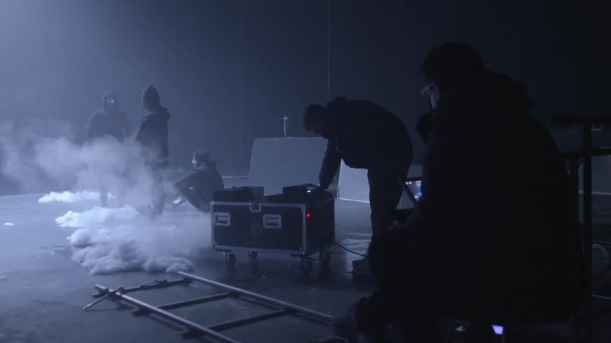 Filmmakers setting up a scene inside a dark smoky warehouse