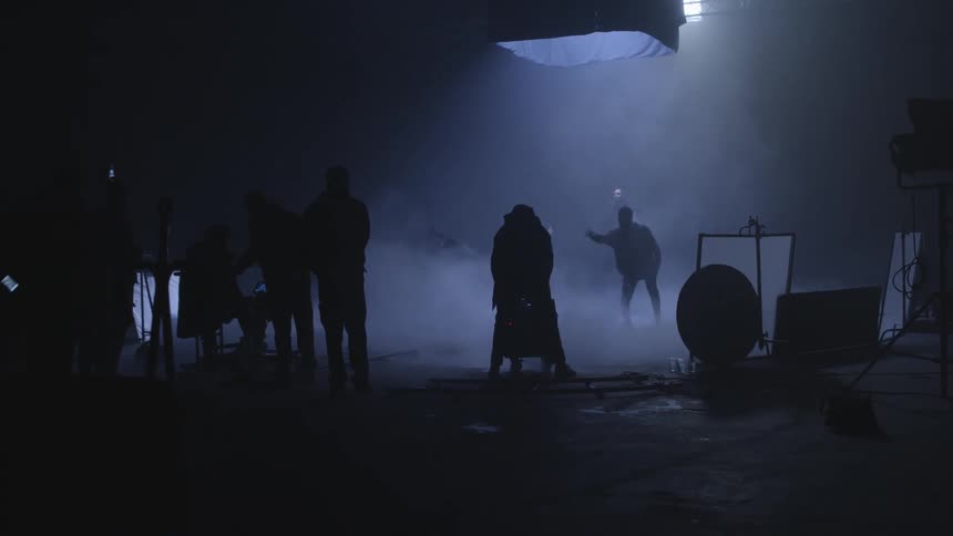 People dance on a dark stage as they are filmed