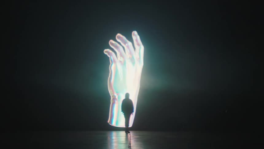 An artist standing in front of a rotating hand image