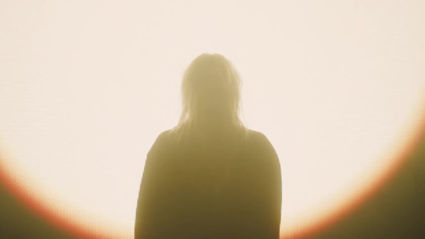 A silhouette of a woman on a stage with a jacket in front of a light