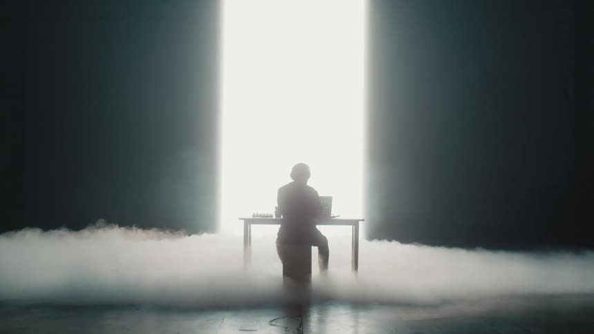 A person on a stage with headphones sitting at a table with a laptop