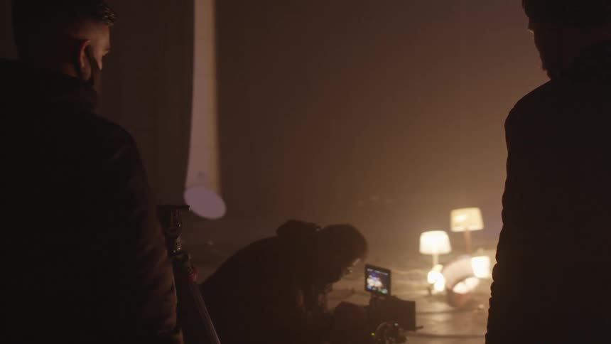 Photographer holding a camera filming lamps scattered around the floor in a photoshoot while two men watch