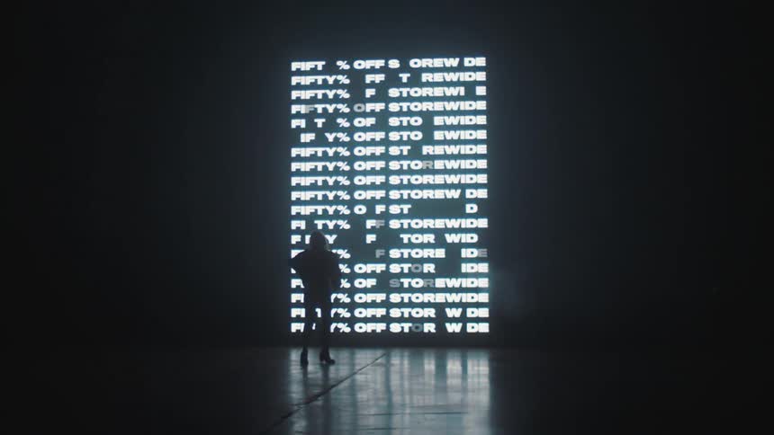 A silhouette of a woman on a stage with a big screen with words in the background