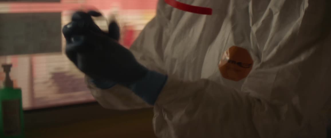 A person in a room with gloves and a face shield applying hand sanitizer on the gloves