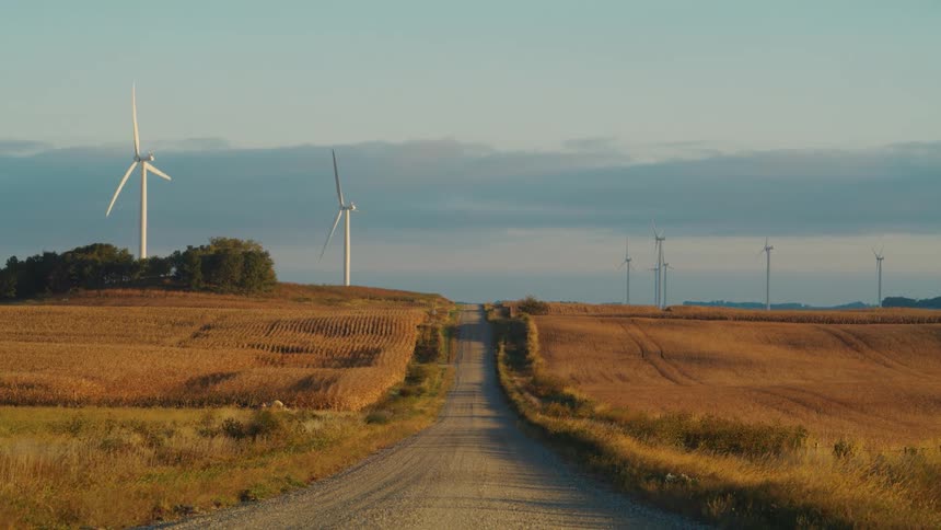 On a farmland country road a turbine on a wind farm turns on a cloudy day