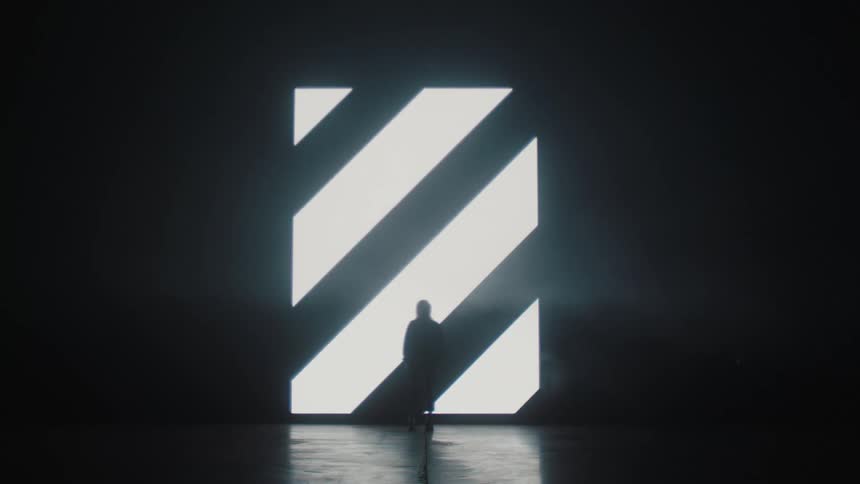 A silhouette of a person standing on a stage with a big screen in the background