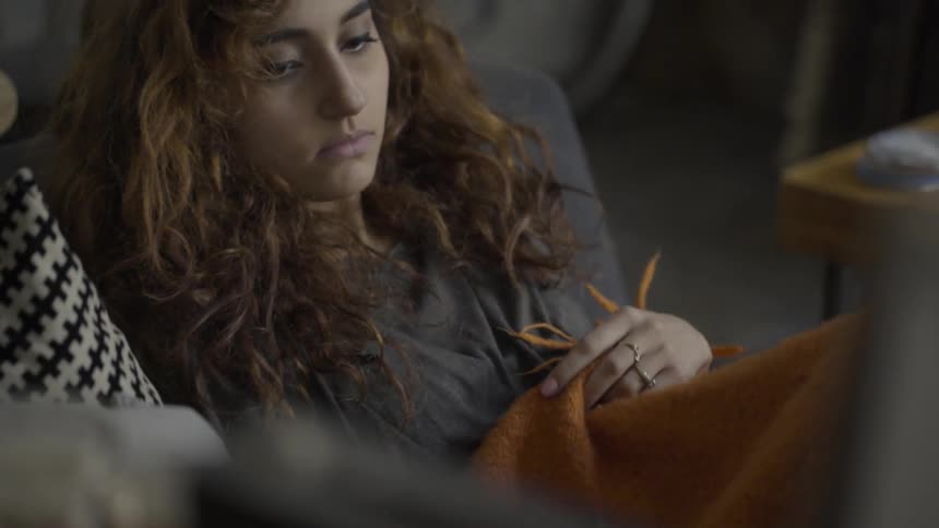 A woman sits down on the couch and puts a blanket on herself