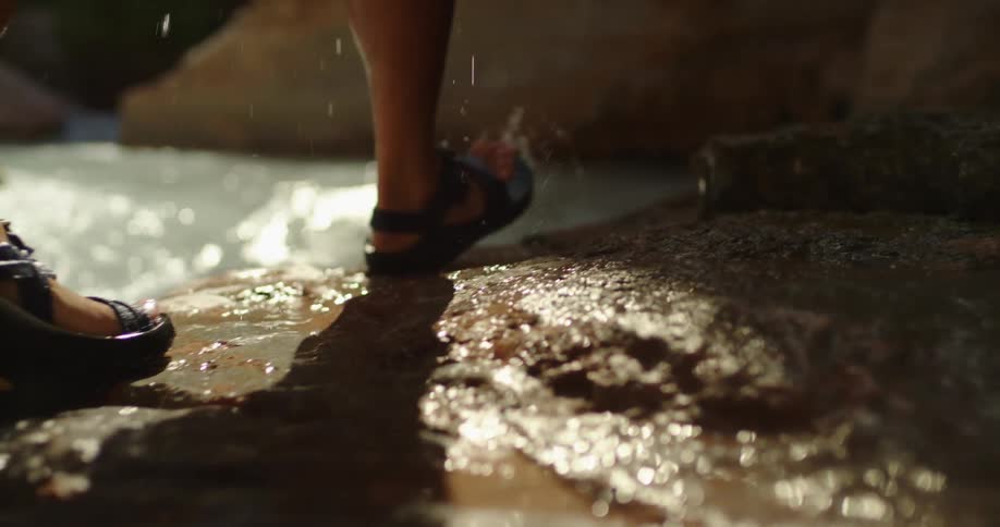 A man wearing sandals dripping with river water as he hikes upstream along a turquoise colored creek deep in Grand Canyon National Park along the Colorado River