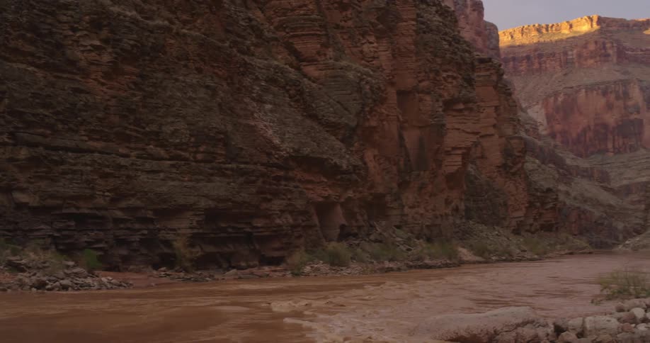 Slow pan right to left ending on a sunrise cliff with the muddy Colorado River flowing deep into the Grand Canyon at sunrise