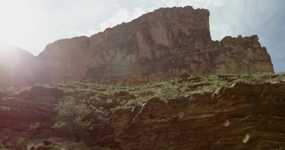 The sun flares as the camera moves downstream while looking up at the north rim of the Grand Canyon of the Colorado River in Arizona