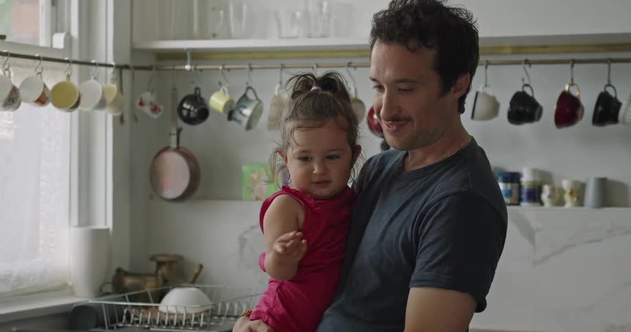 Father holds daughter on his arms talking on a video call on a laptop in the kitchen