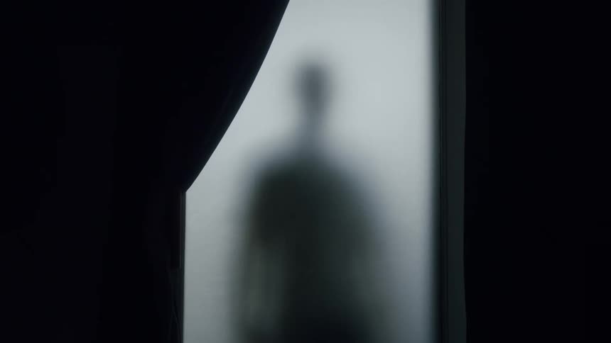 Silhouette of an out of focus person standing behind a glass