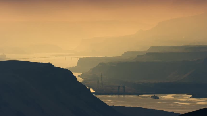 A surreal foggy landscape with the Columbia River gorge being lit up by sunrise light on a foggy moody morning with bridges and barges on the river