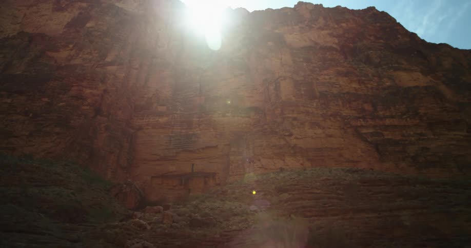 Looking up at the rim of the Grand Canyon from deep in the river bottom as the lens flares in the morning sunrise sky