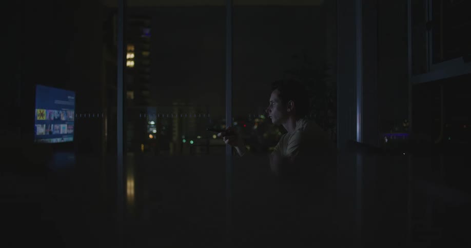 A man sitting around at night watching tv