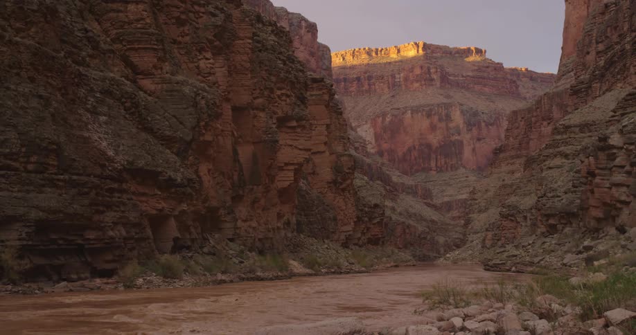 Static shot of the muddy Colorado River flowing deep into the frame at sunrise in Grand Canyon National Park in the American Southwest