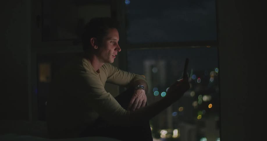 Man sitting in bed greets someone on a video call in his smartphone at night