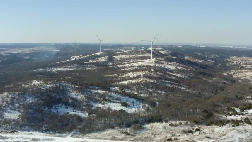 Aerial view of wind turbines spinning on the snow covered hills at daytime
