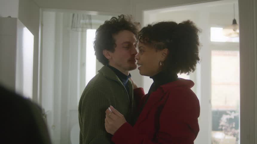 A man and a woman in a room hugging with the woman with a pregnancy test in her hand