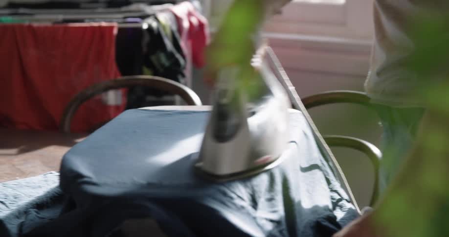 A man ironing clothes with a steaming iron over an ironing table at home