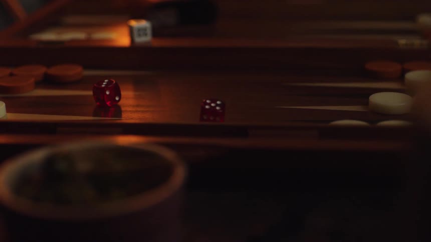 Red dice are dropped onto a wooden backgammon board