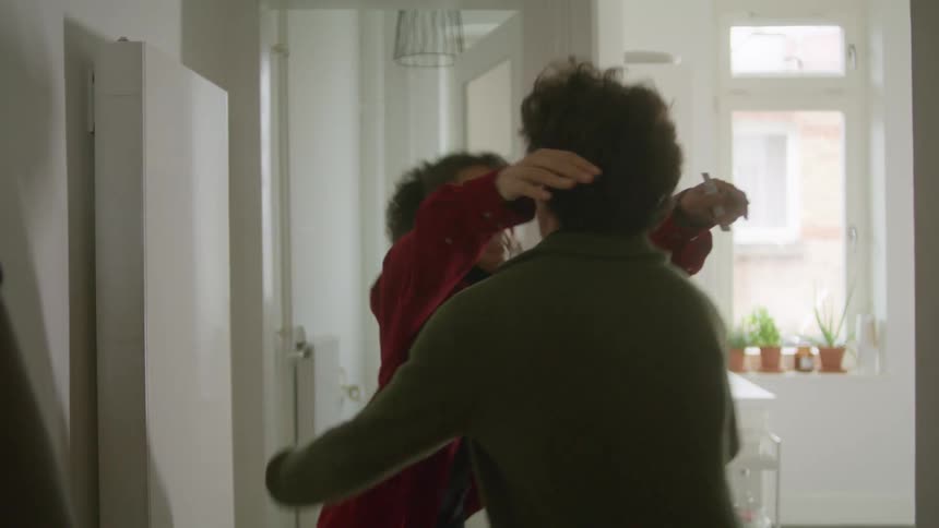 A woman exits from a bathroom at home while holding a pregnancy test smiling as a man walks over to her and they embrace