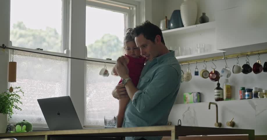 Father carrying daughter helps her wave at laptop video call
