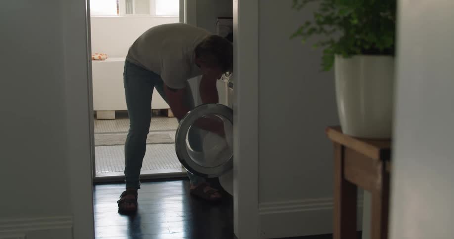 Man walking into laundry room and loading laundry into front loader