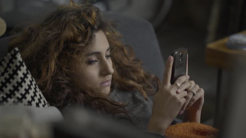 A woman laying on a sofa looking at a smartphone