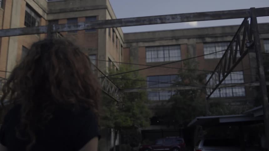 A woman standing near buildings looking up towards the sky