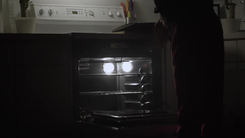 A woman removing a cookie sheet from an oven