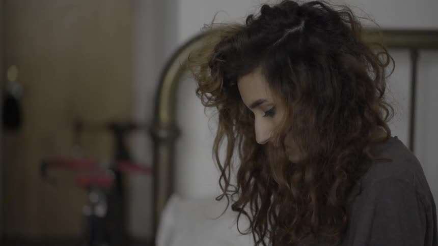 A woman looks down while sitting on a bed