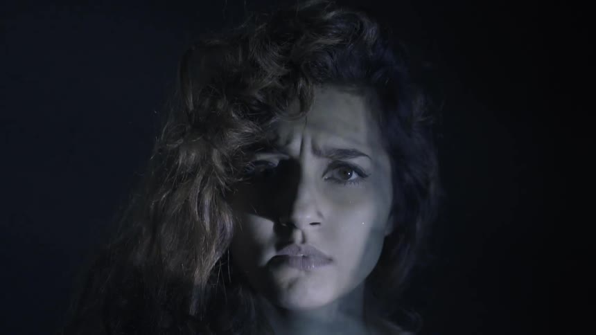 A woman licks her lips in a dark room