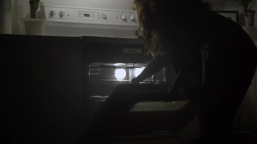 A woman places a cookie sheet with loaves on it into an oven