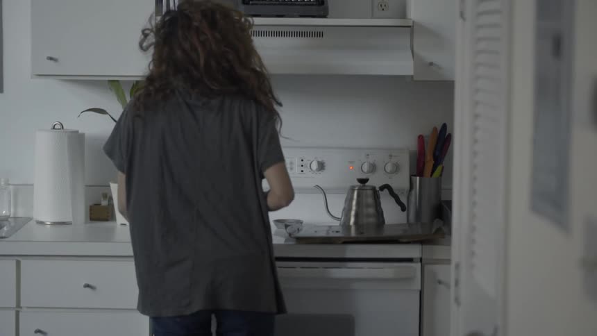 A girl walks into a kitchen to grab a kettle pot