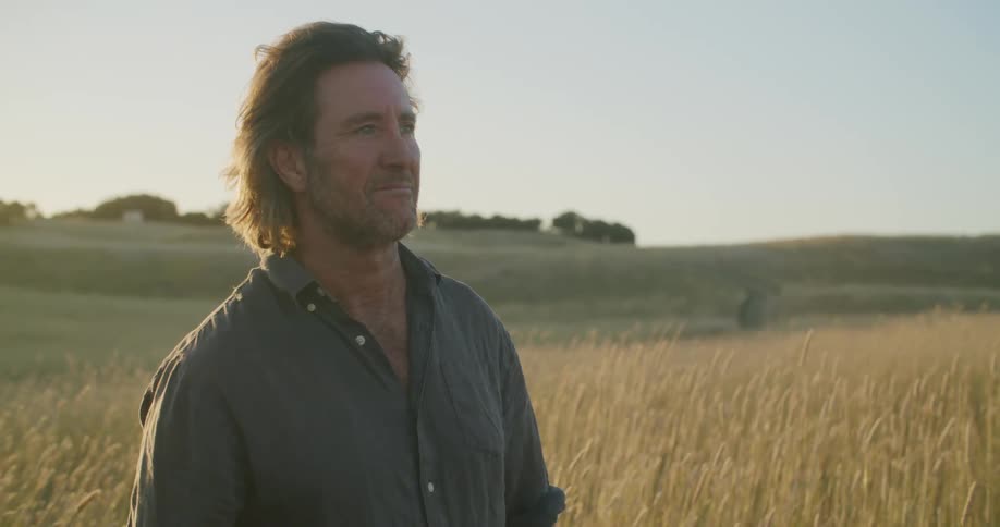 A man is standing outdoors in a rural area at dusk