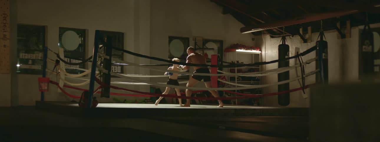 A young boy trains with an older man as they box in a boxing ring
